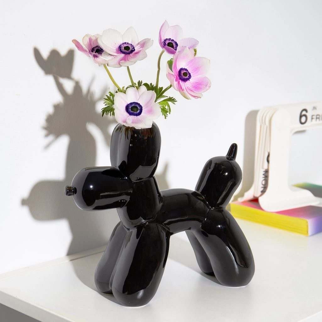 Black balloon dog-shaped vase with flowers on a white surface