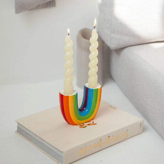 Colorful rainbow-shaped candle holder with three candles on a white surface.