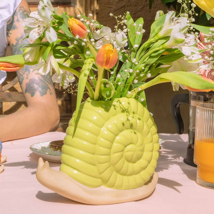 Snail-shaped vase with flowers on a table outdoors